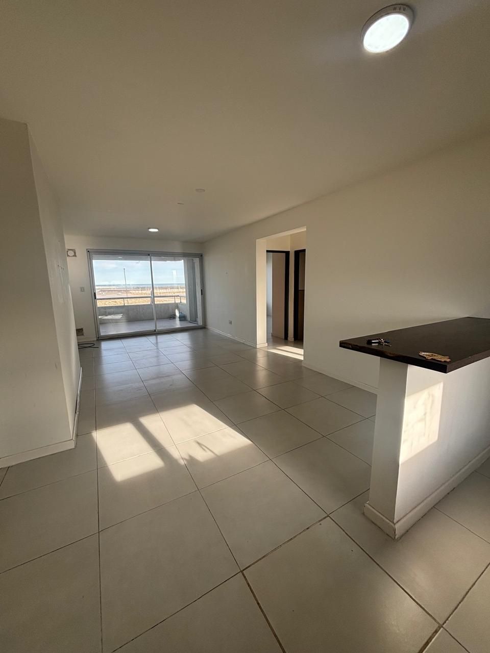 Living-comedor amplio con piso cerámico, mirando hacia el balcón con vista a la costa