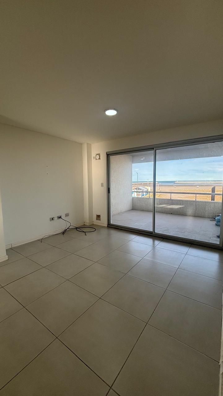 Living-comedor con la puerta ventana abierta al balcón, y a lo lejos la costa y el mar